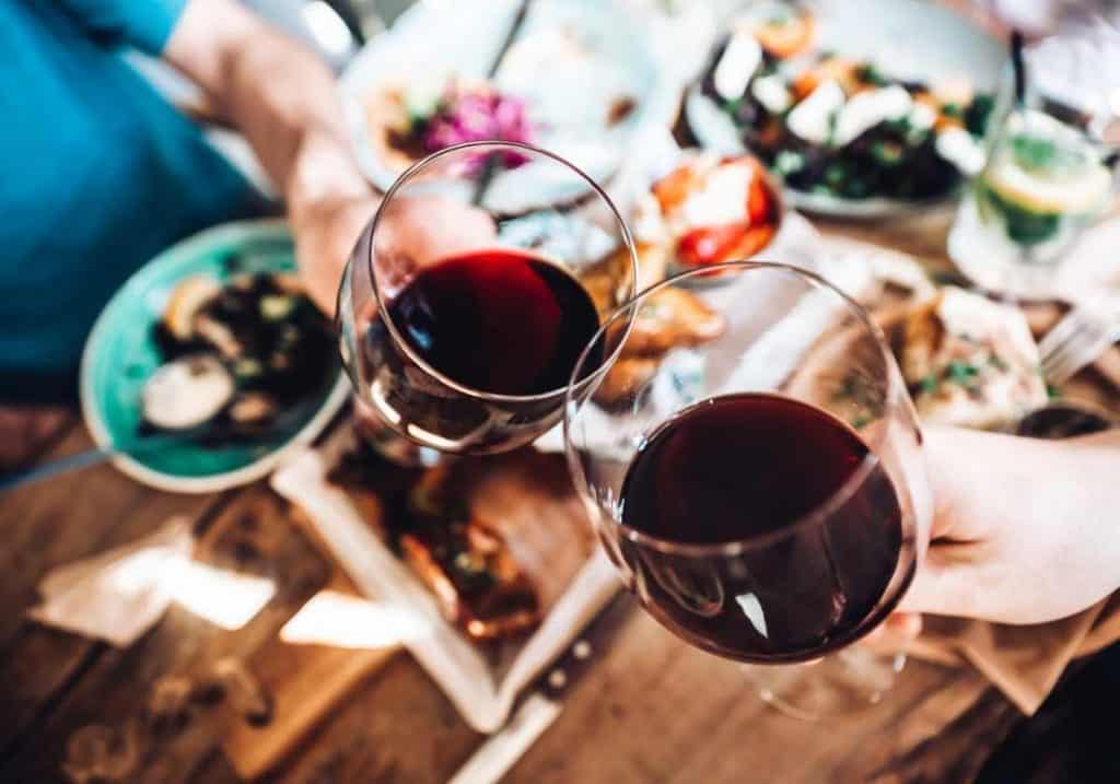 2 glasses with red wine over a spread of food