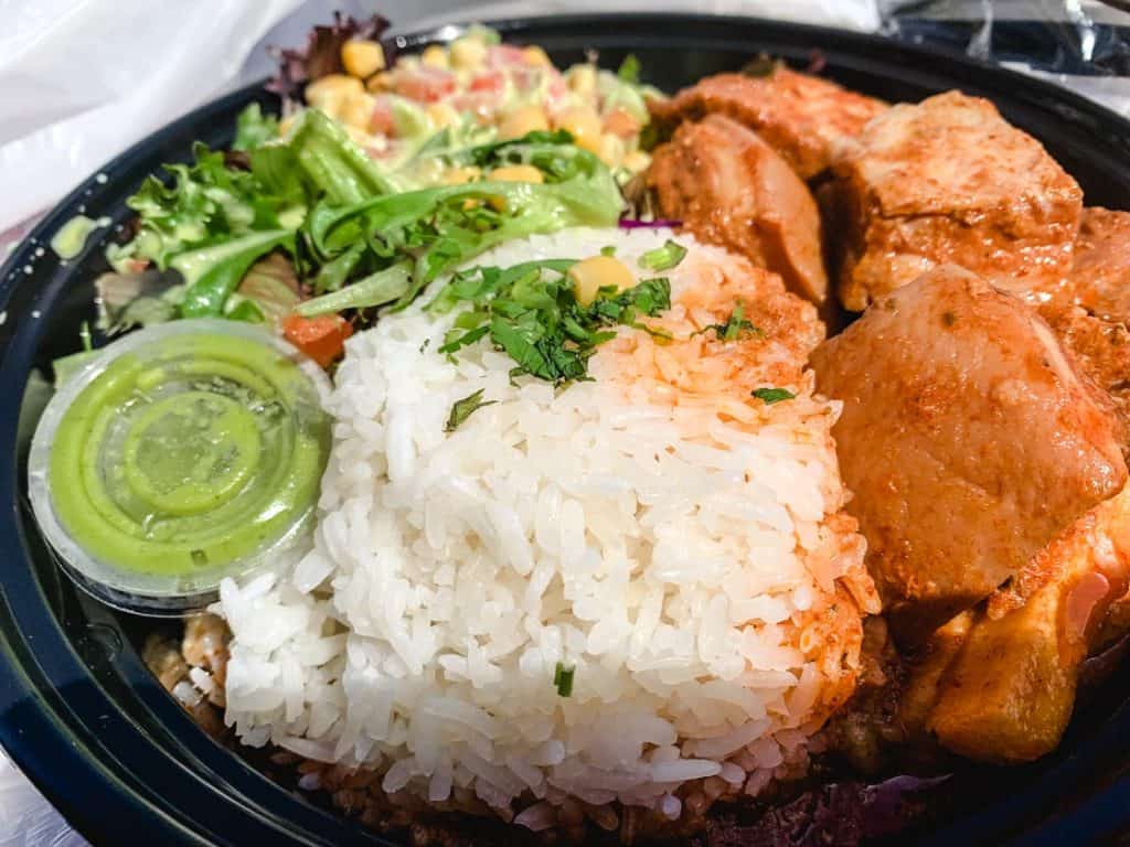 peruvian pork belly with white rice and salad in a black takeout box