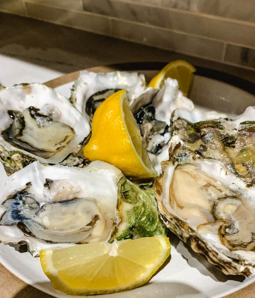 plate of oysters on the half shell with lemon wedges