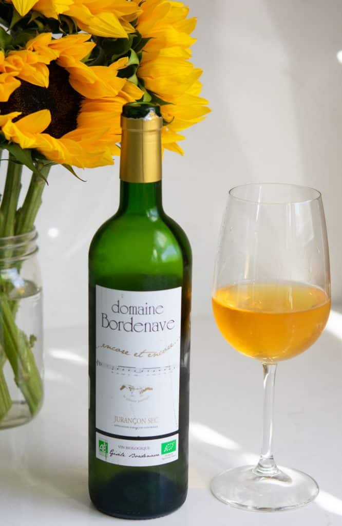 2019 Domaine Bordenave Jurancon Sec wine bottle and glass with sunflowers in the background