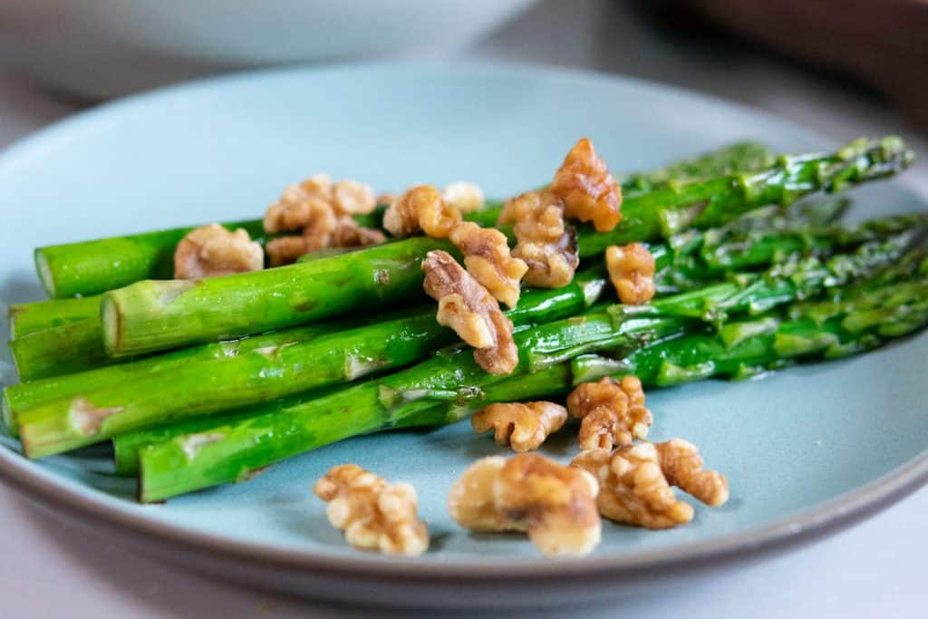 roasted asparagus spears on a blue plate with walnuts