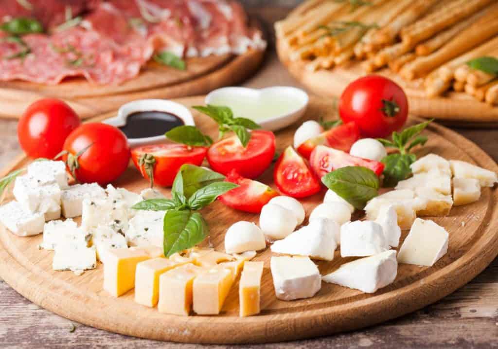 Cheese cubes on a round wood cutting board with chopped tomatoes