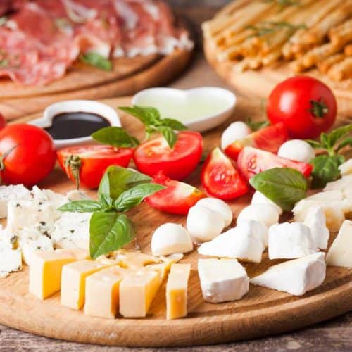 Cheese cubes on a round wood cutting board with chopped tomatoes