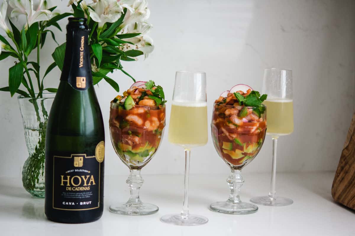 2 glasses of of cava with a wine bottle and 2 goblets of Mexican shrimp cocktail