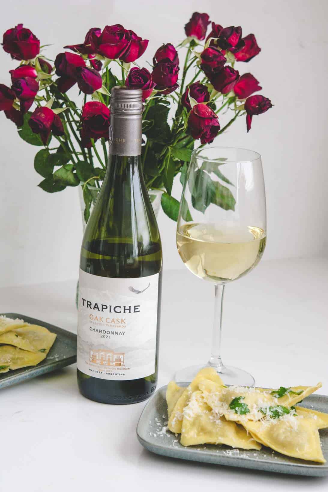 Bottle and glass of Trapiche Chardonnay with a gray rectangular plate of ravioli with grated pecorino cheese and parsley