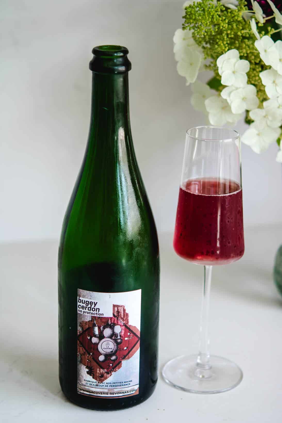 Glass and wine bottle of Bugey Cerdon sparkling wine with white flowers in the background
