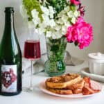 Wine bottle and glass of bugey cerdon with french toast and bacon with flowers in the background