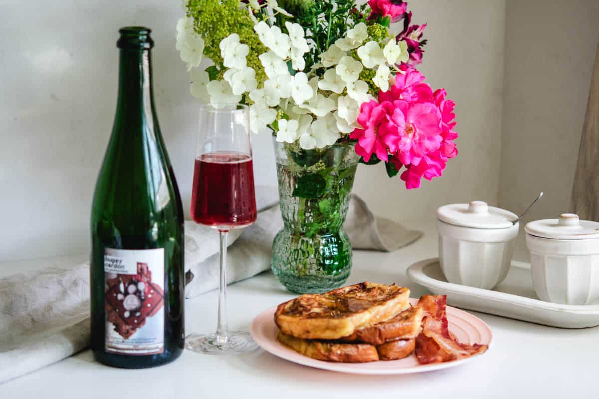 Wine bottle and glass of bugey cerdon with french toast and bacon with flowers in the background