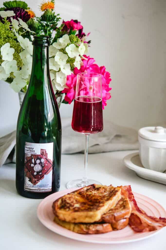 Wine bottle and glass of bugey cerdon with french toast and bacon with flowers in the background