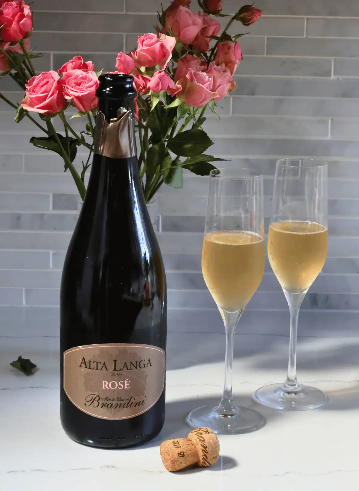 Alta Langa wine bottle and 2 glasses of wine with pink roses in the background