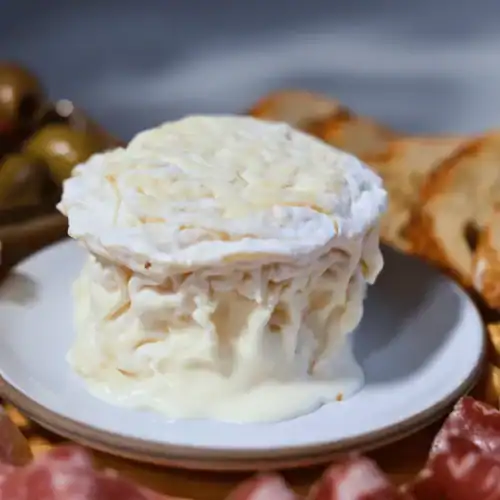 La Tur Cheese round on a white plate surrounded by charcuterie board