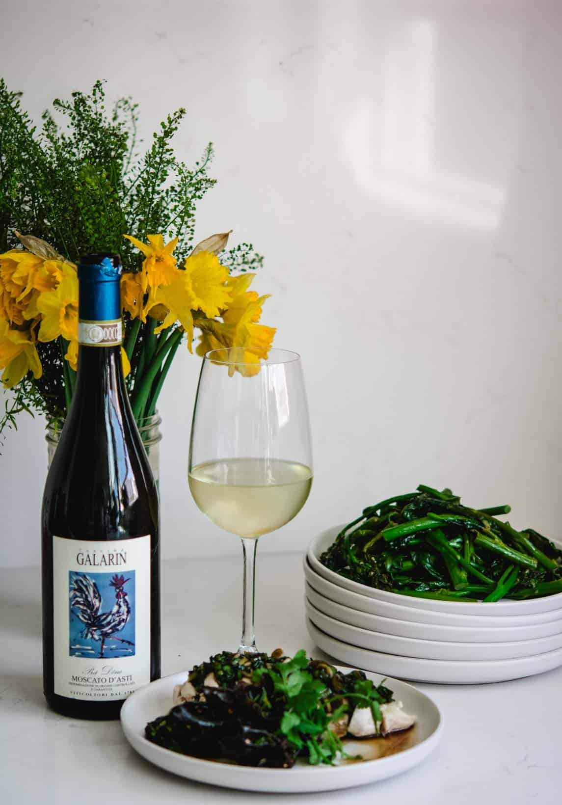 Wine and fresh green vegetables with a glass of white wine on a white table.