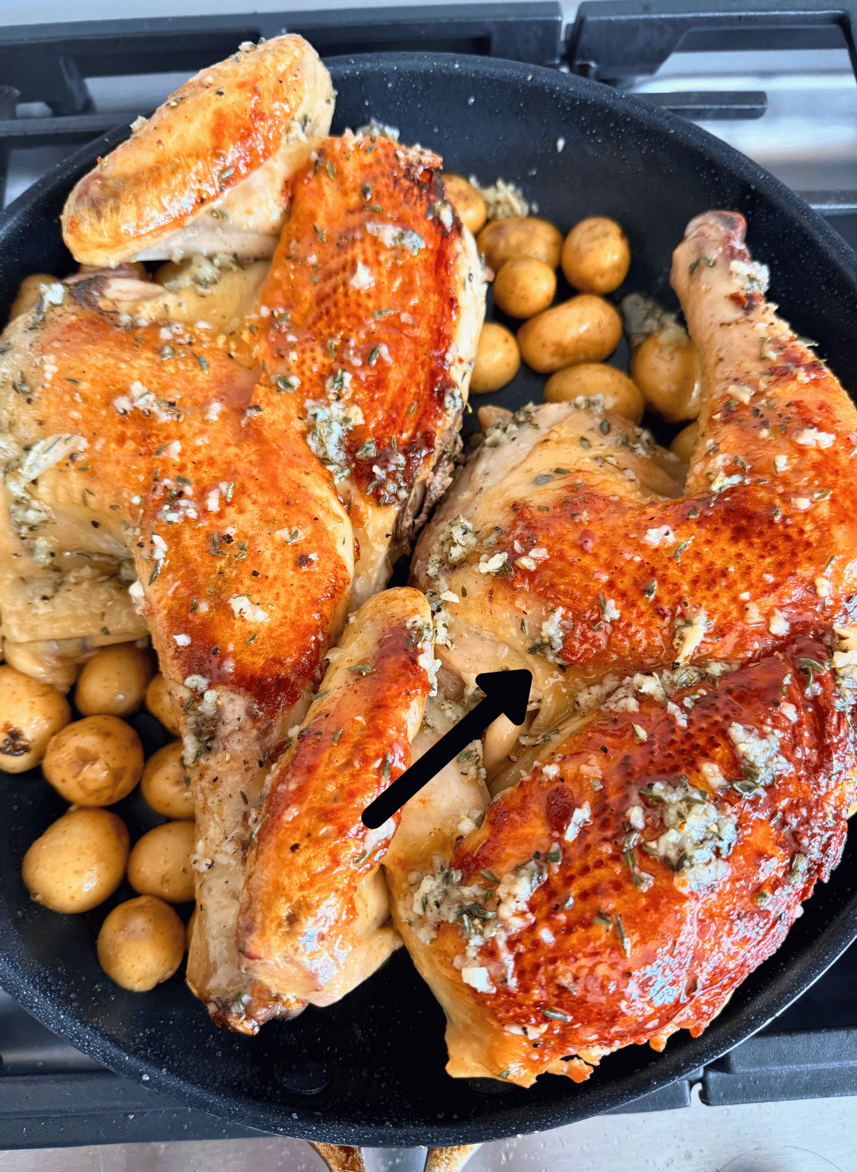 Chicken under a brick in a black pan with baby potatoes