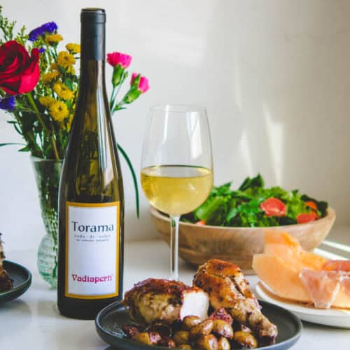 Gourmet meal with wine, flowers, and fresh salad on a white table.